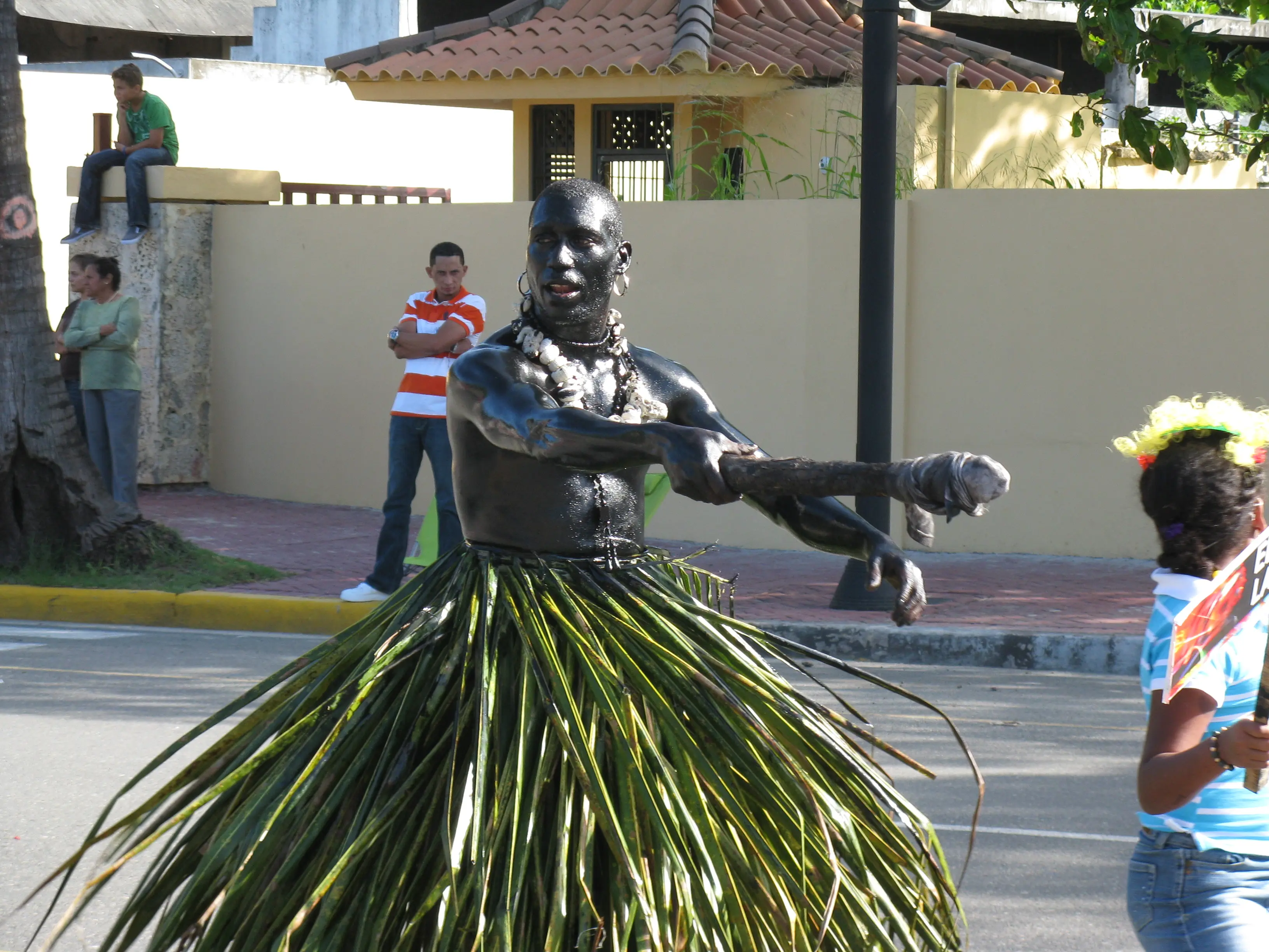 Carnaval performer painted black with a palm leaf skirt dancing in the street