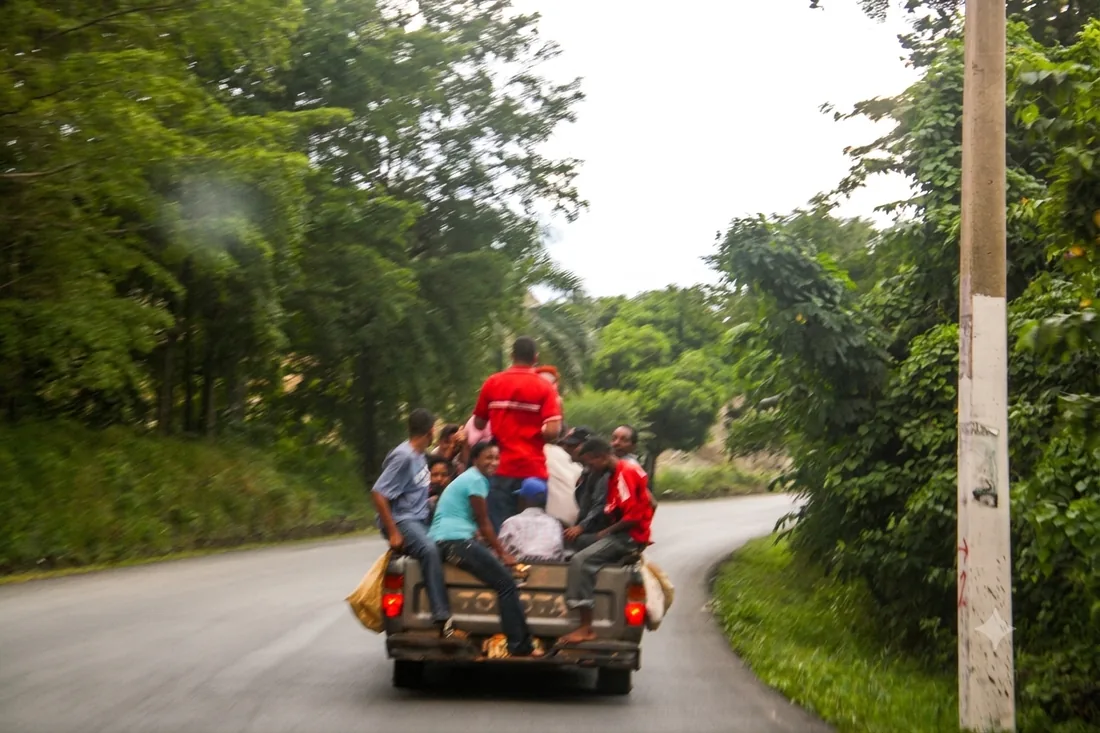 Family riding in the back of a pickup truck on a rural road in the Dominican Republic, a common form of local shared transport