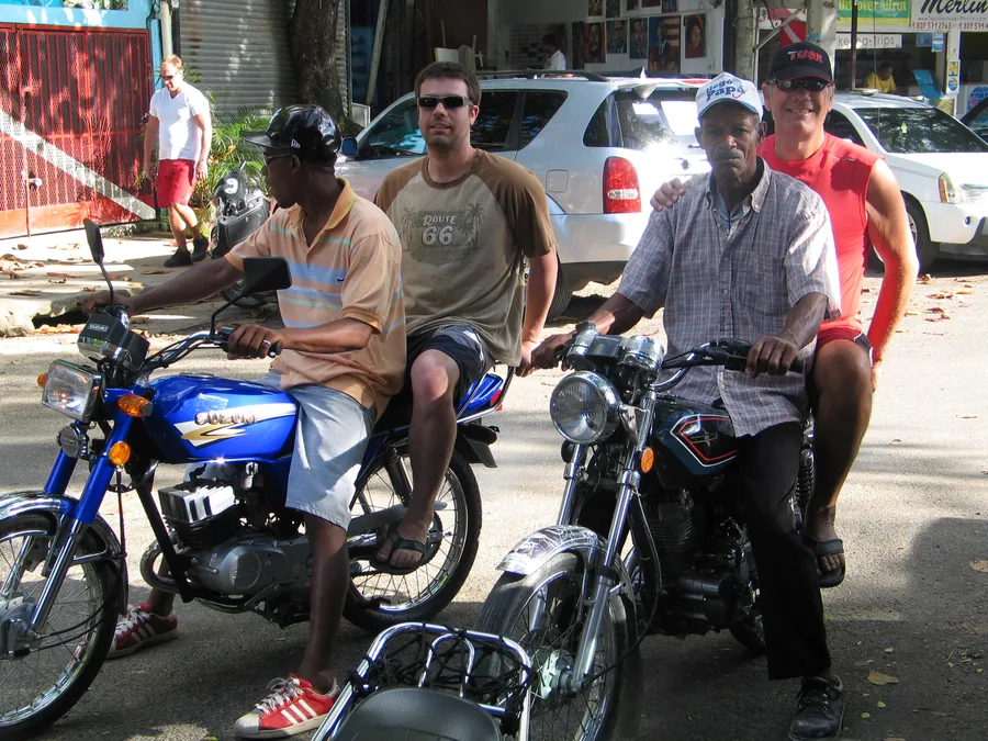 Two motoconcho drivers with passengers on motorcycles on a street in Puerto Plata