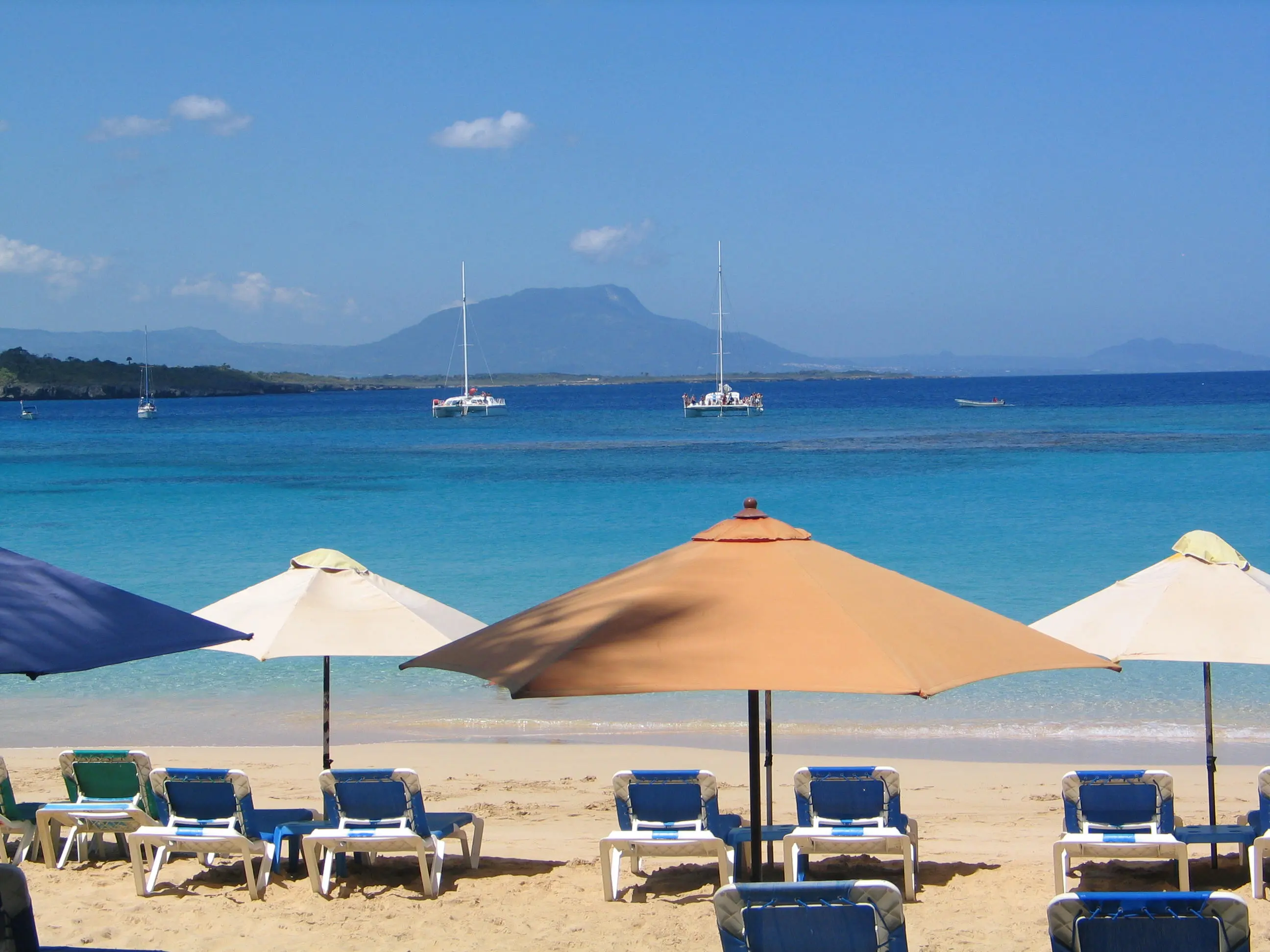 Beach loungers and umbrellas at Sosúa with catamarans and mountain in background
